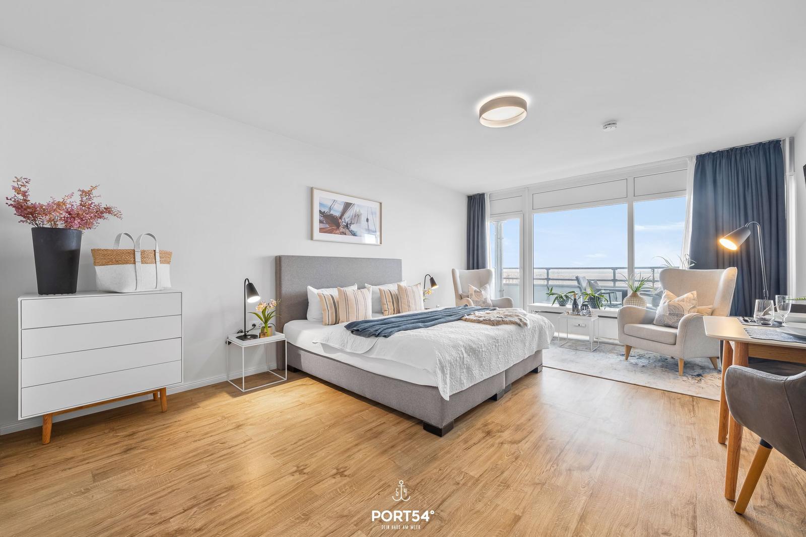 Schlafzimmer mit Balkon, Bett, Schrank und Sitzgelegenheiten.