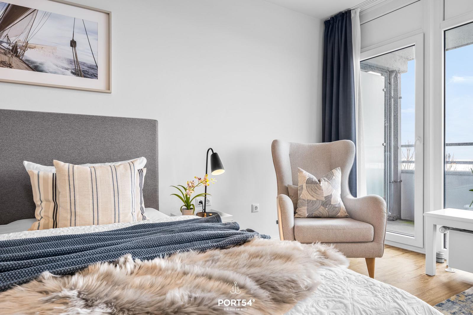 Schlafzimmer mit Bett, Sessel und Blick auf Balkon.