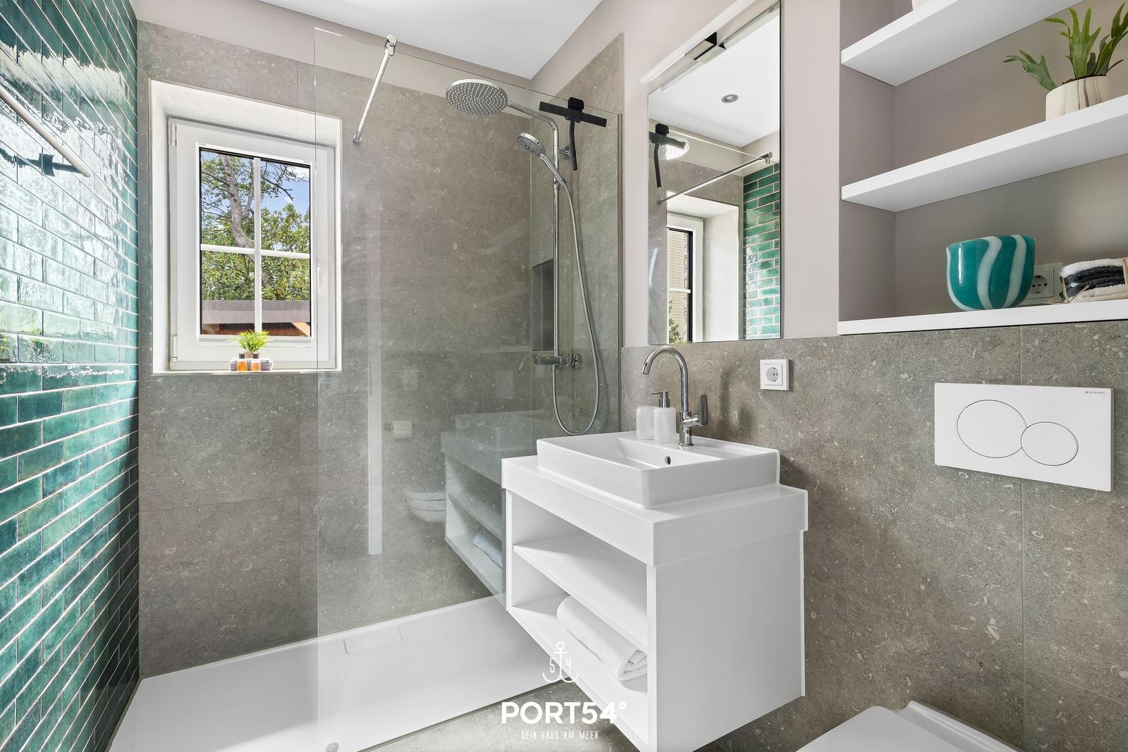 Badezimmer mit Dusche, Waschbecken und Fenster mit Blick nach draußen.