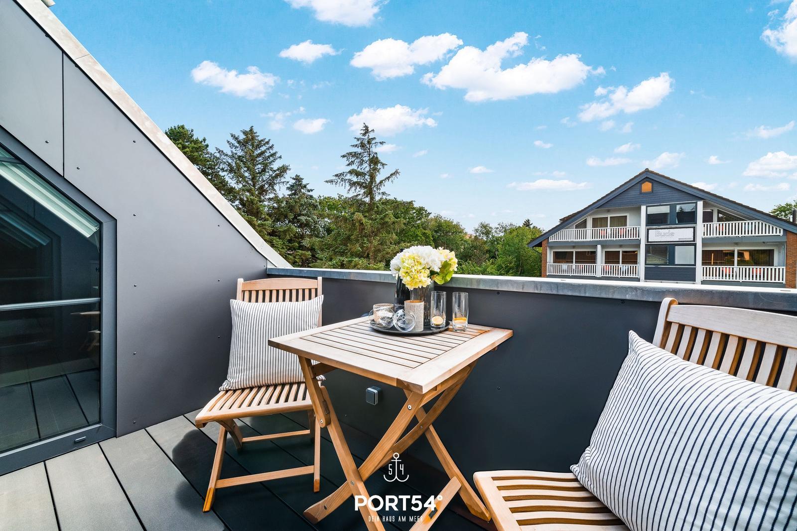 Terrasse mit Holztisch und Stühlen, Blick auf Wald und Haus.
