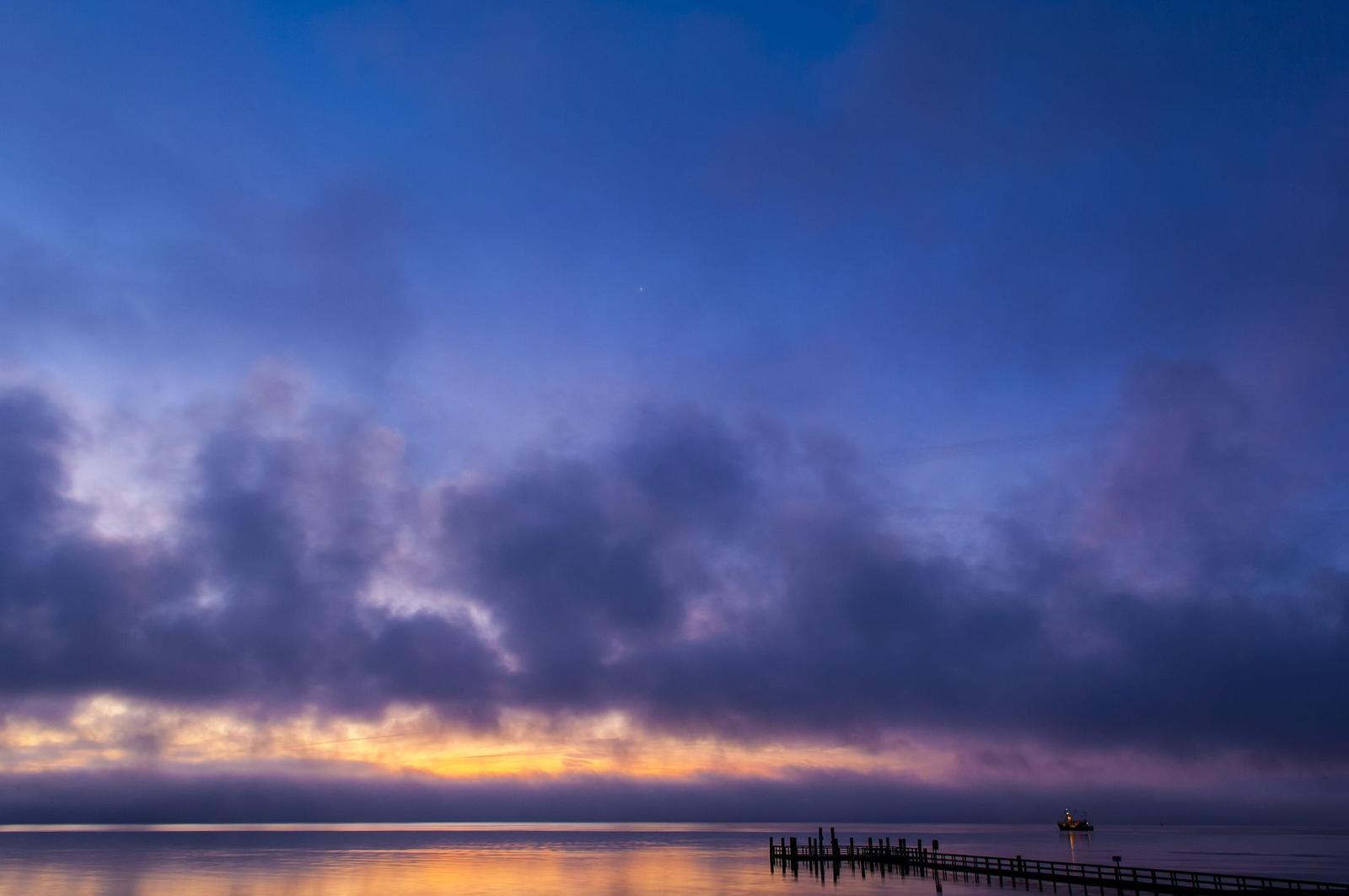Sonnenuntergang über dem Wasser mit einem Pier und einem Boot.