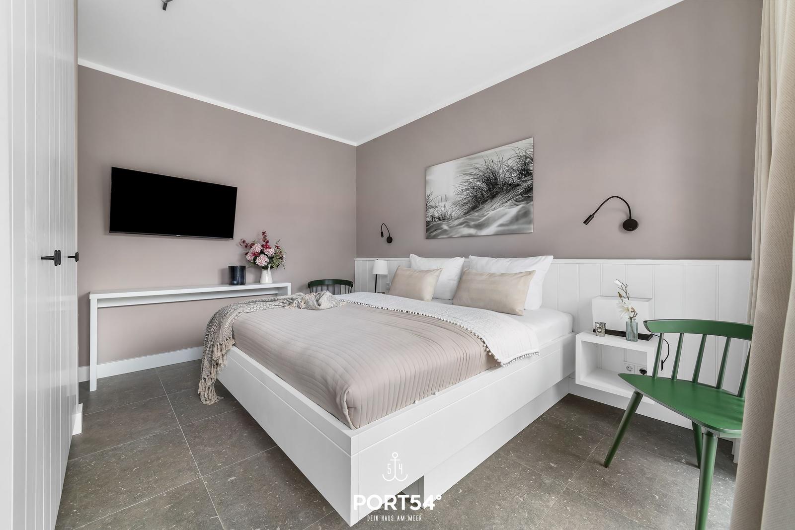 Schlafzimmer mit Bett, Fernseher und grüner Stuhl.