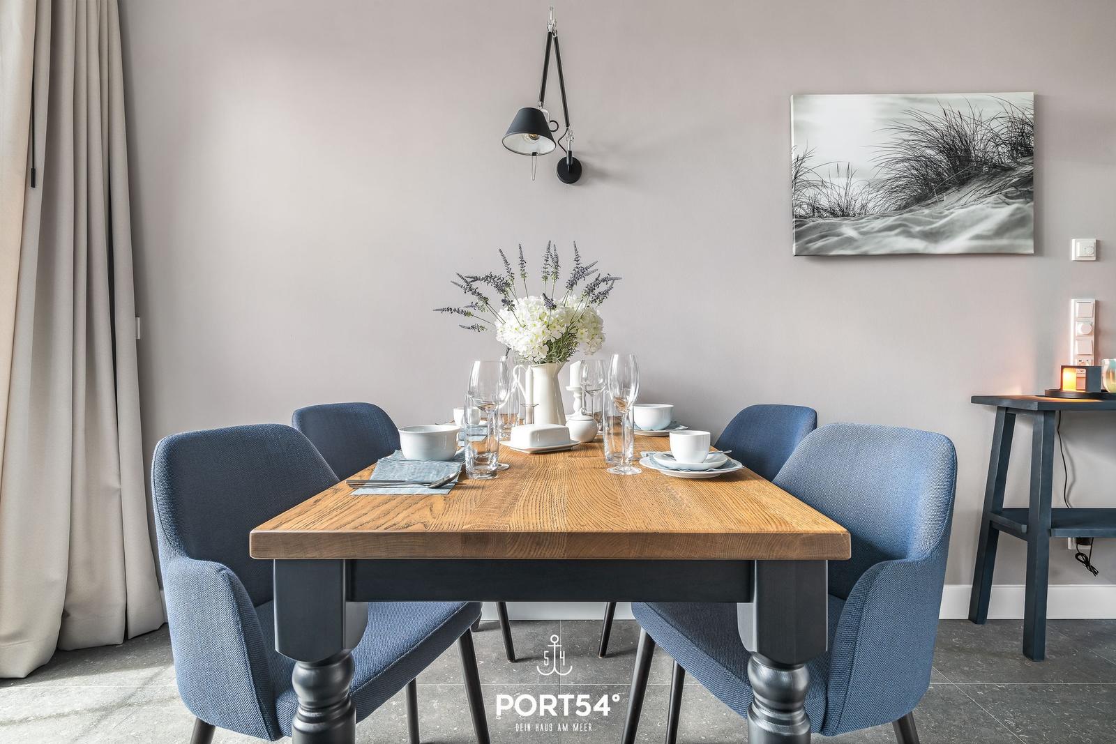 Esstisch mit sechs Stühlen, Blumen und Wandbild mit Dünenmotiv.
