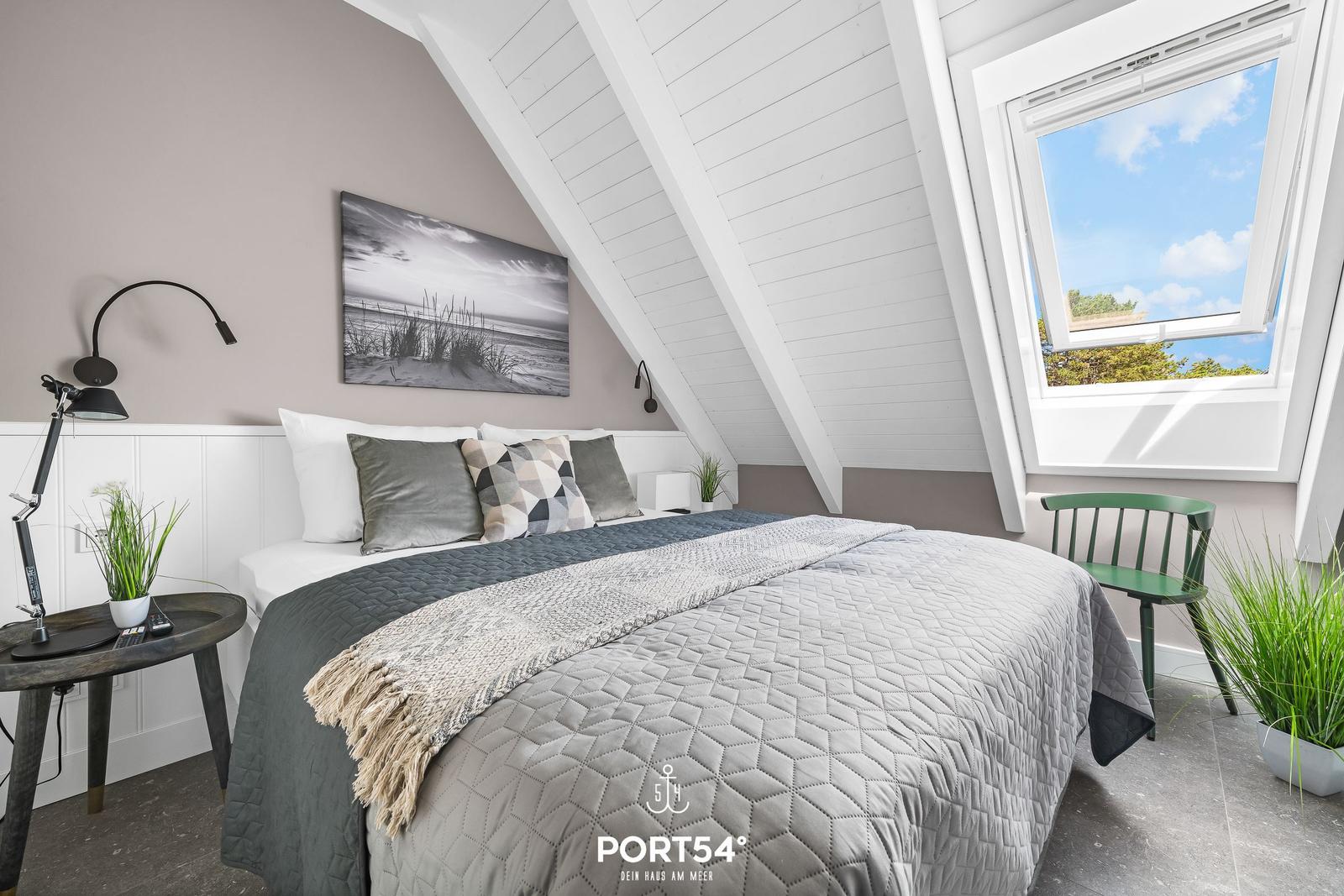 Schlafzimmer mit Dachschräge, Fenster und Bett mit Decke.