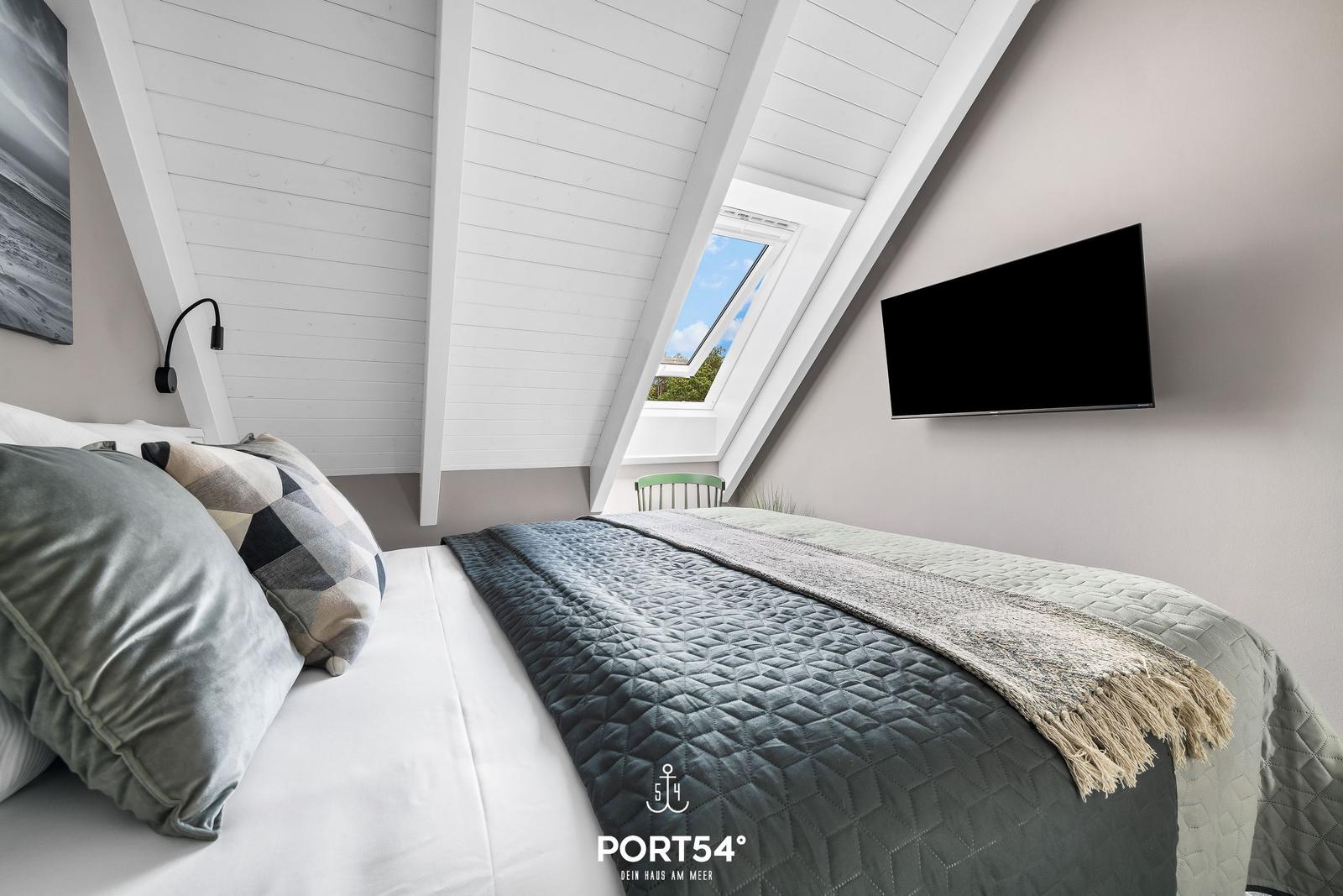Schlafzimmer mit Dachschrägen, Dachfenster und Wandfernseher.