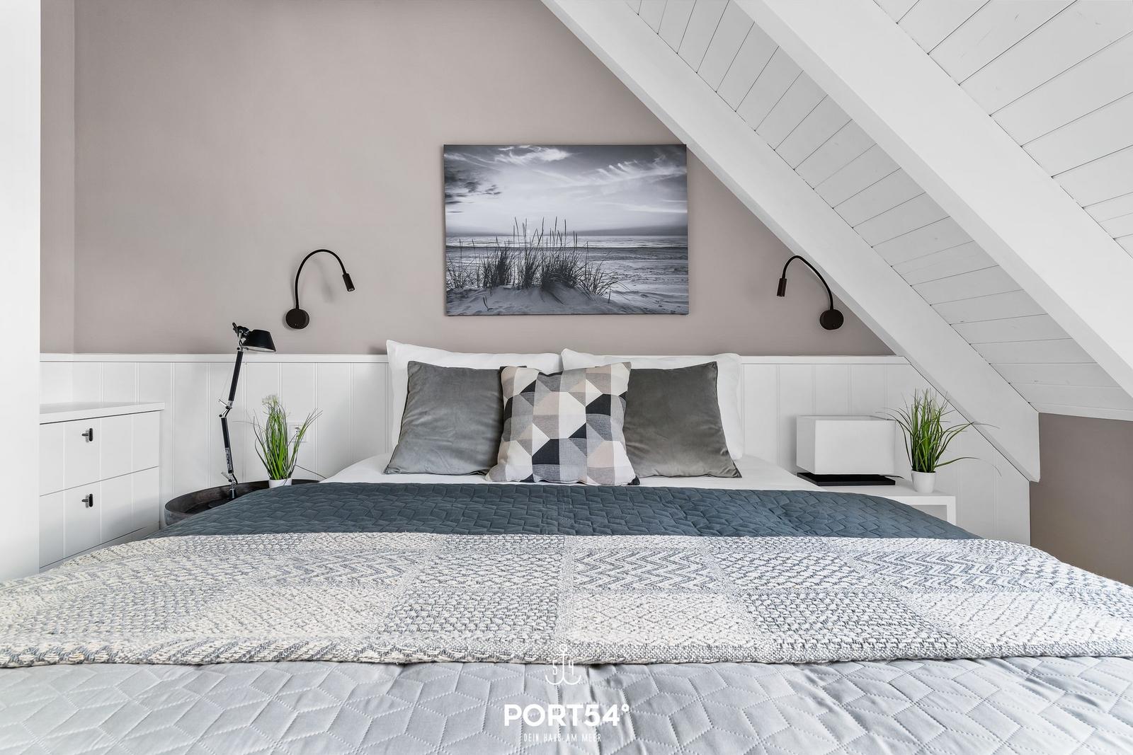 Schlafzimmer mit Dachschräge, Bett mit Kissen und Wandbild.