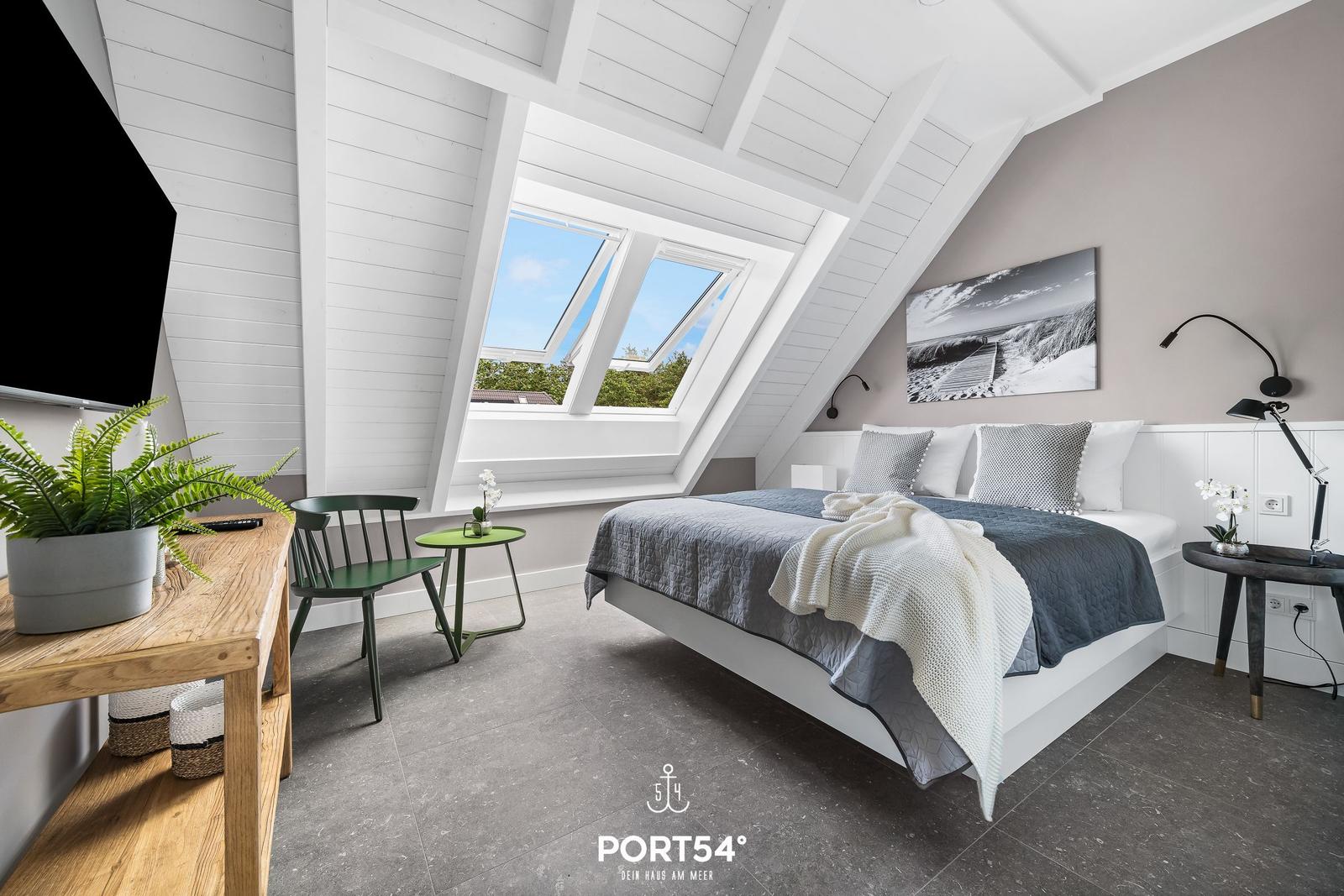 Schlafzimmer mit Dachfenster, Bett, Nachttisch und Fernseher.