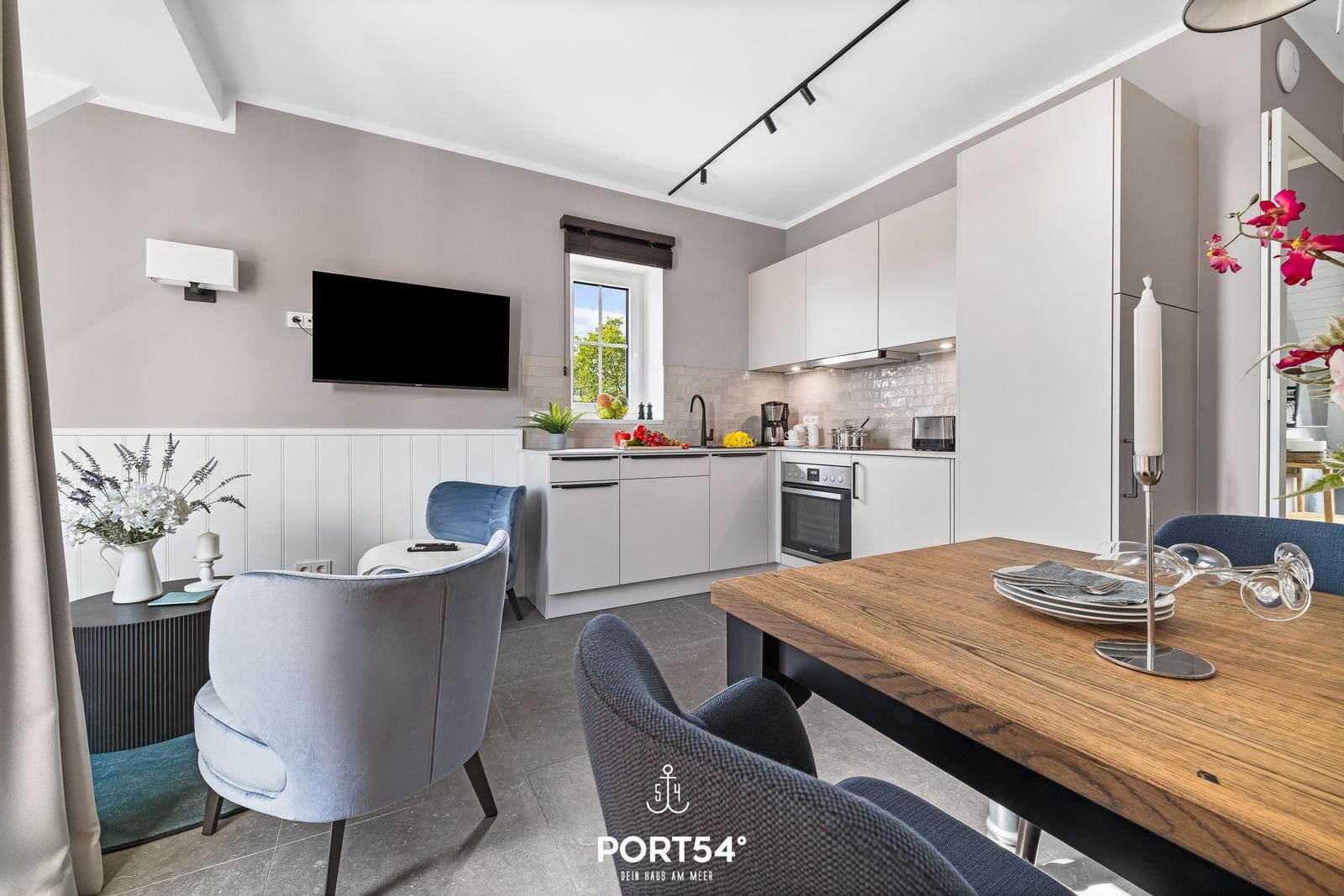 Küche mit Essbereich und Fernseher an der Wand. Holztisch mit Stühlen und Fenster mit Blick.