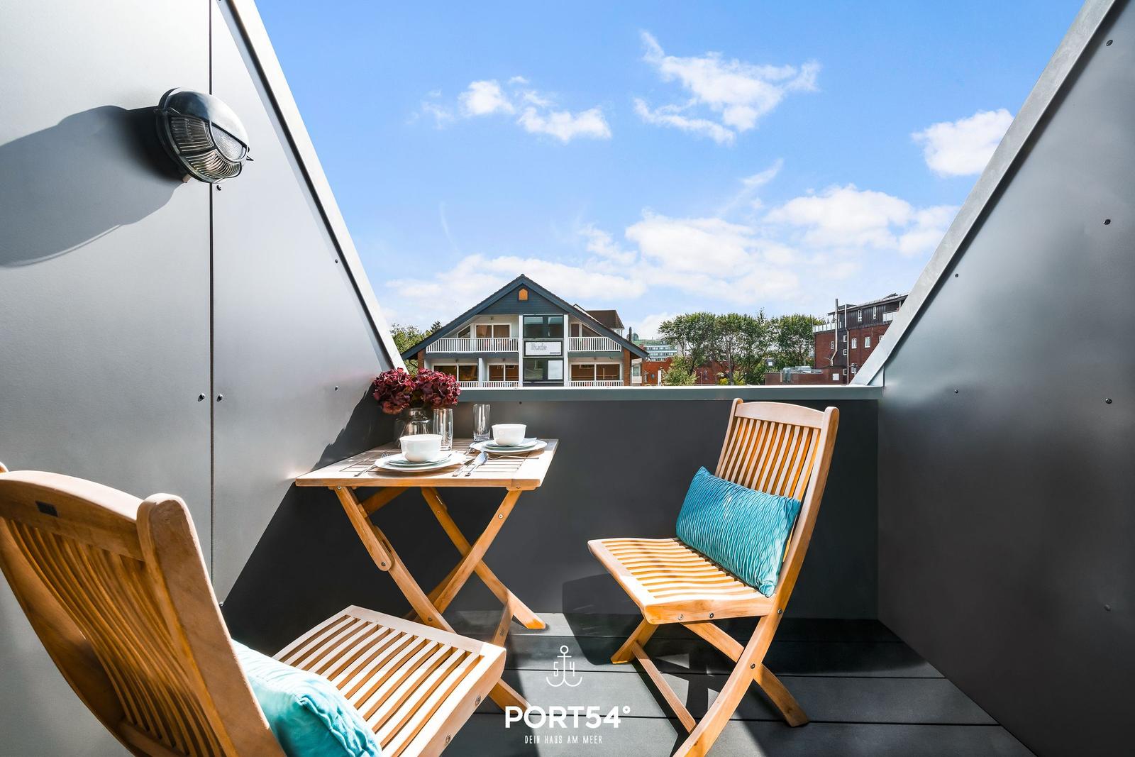 Terrasse mit Tisch und zwei Stühlen, Blick auf Haus und Himmel.