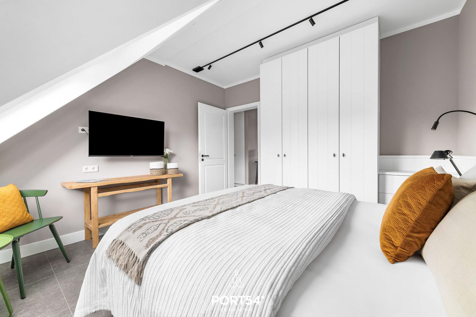 Schlafzimmer mit Dachschräge, Bett, Kleiderschrank und Fernseher an der Wand.
