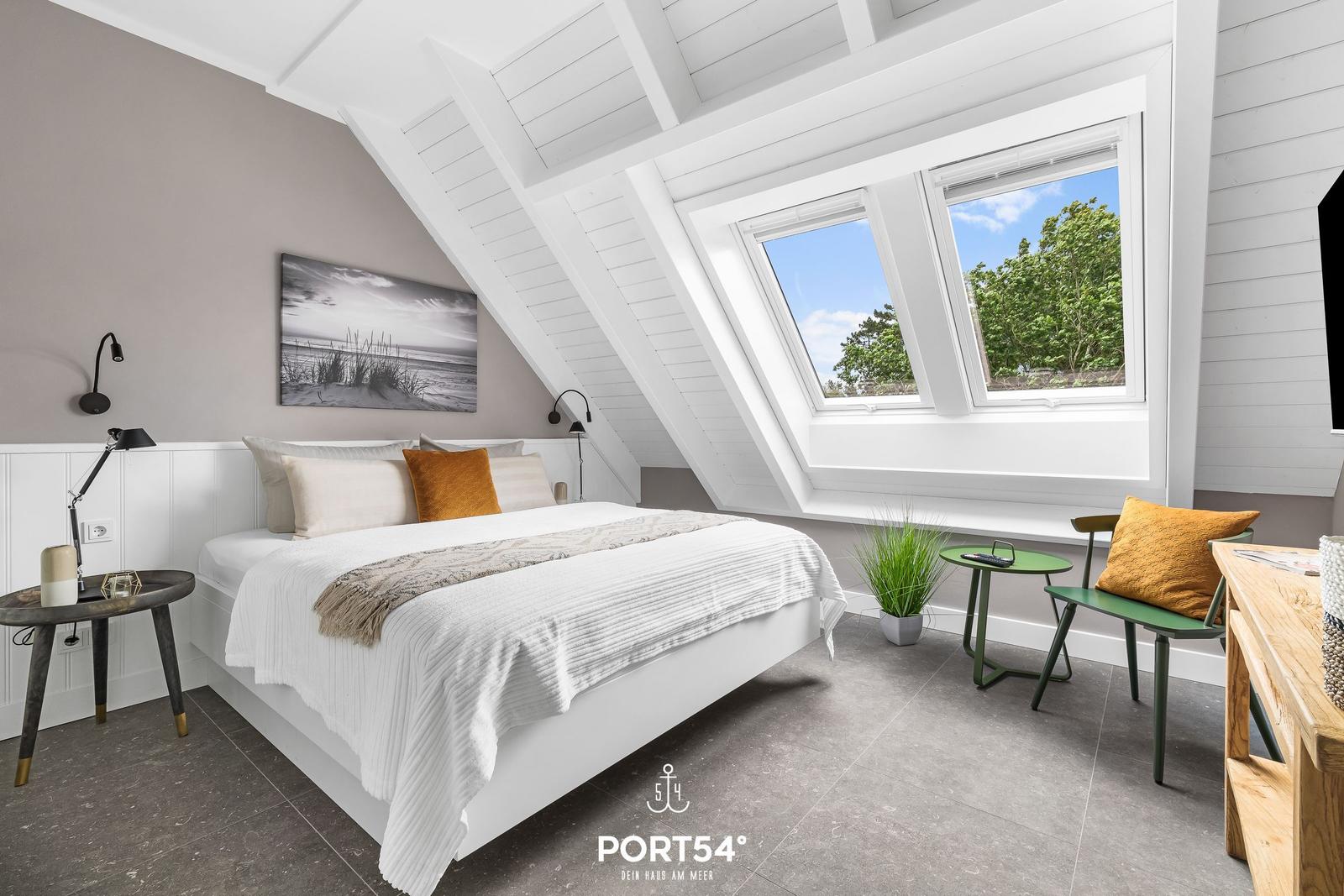 Schlafzimmer mit Dachfenster, Bett, Nachttisch und Sitzgelegenheit.