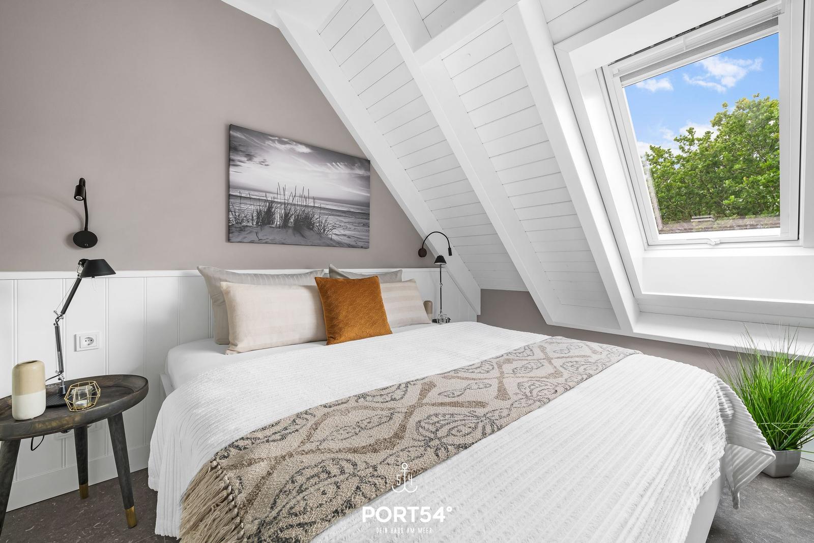 Schlafzimmer mit Dachfenster, Bett, Wandbild und Nachttisch.