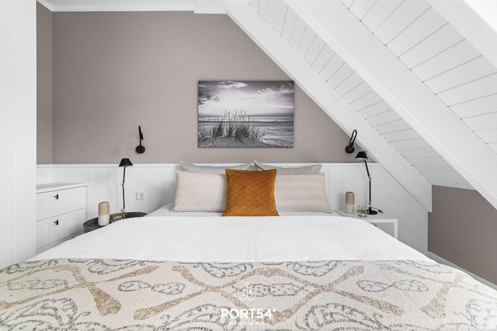 Schlafzimmer mit Dachschrägen, Bett, Kissen und Wandbild.