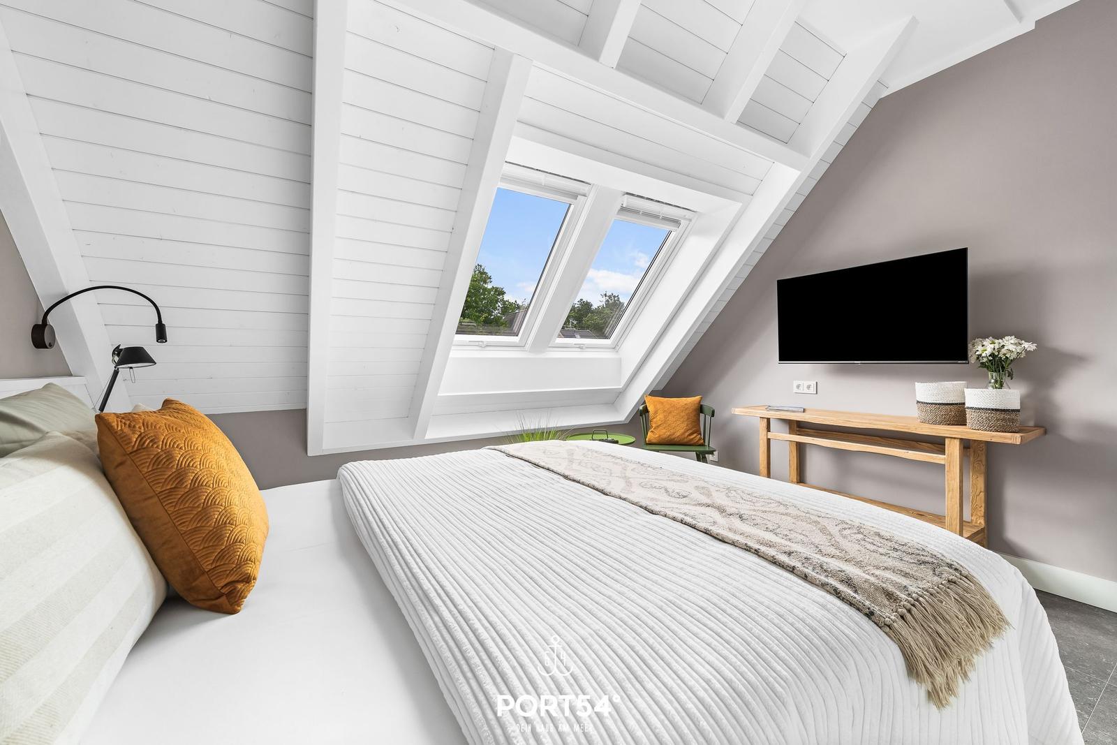 Schlafzimmer mit Dachfenster, Bett, TV und Holztisch.