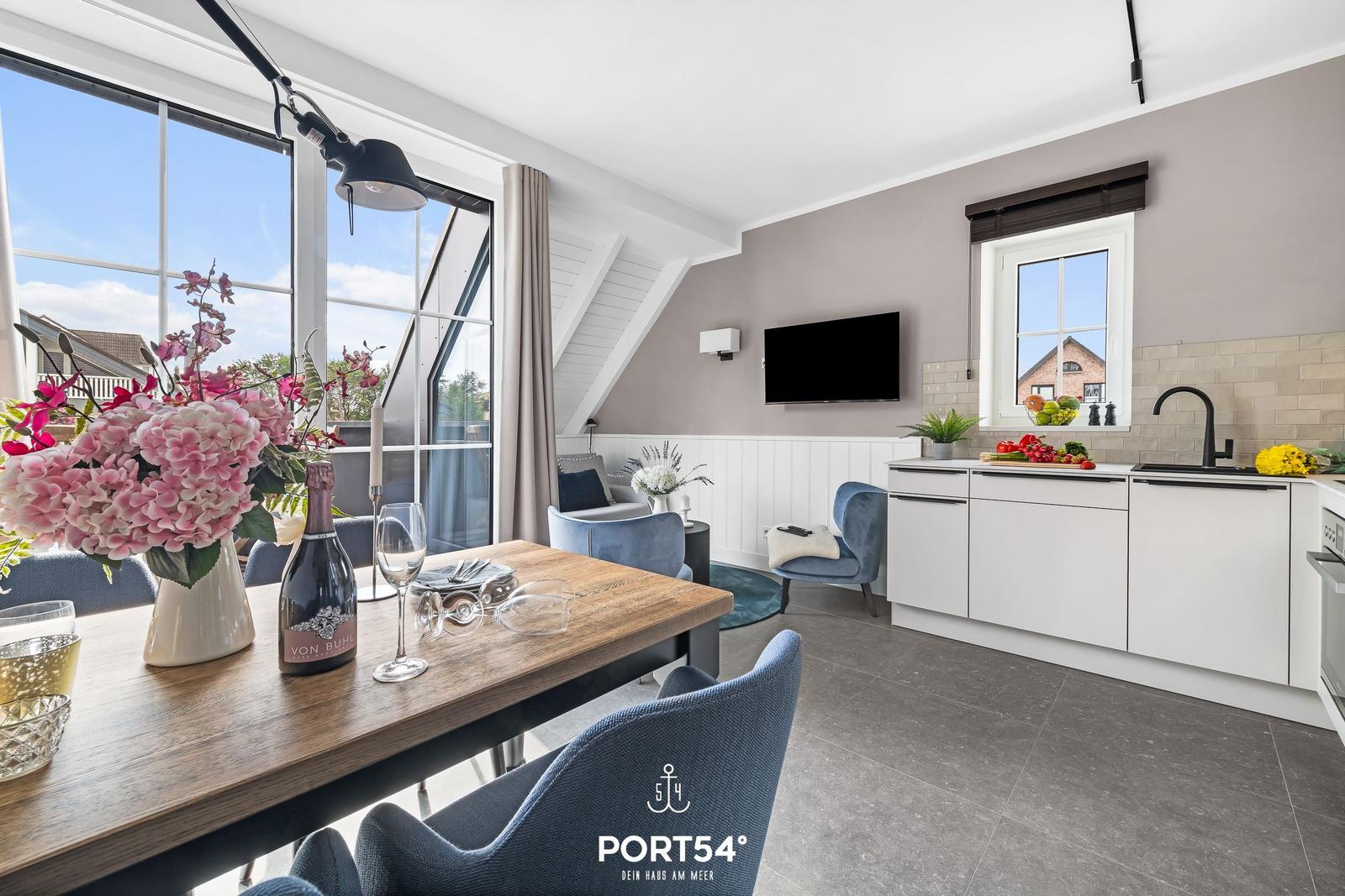 Essbereich mit Tisch, Stühlen und Blick auf Balkon. Küche mit Arbeitsplatte und Fenster.