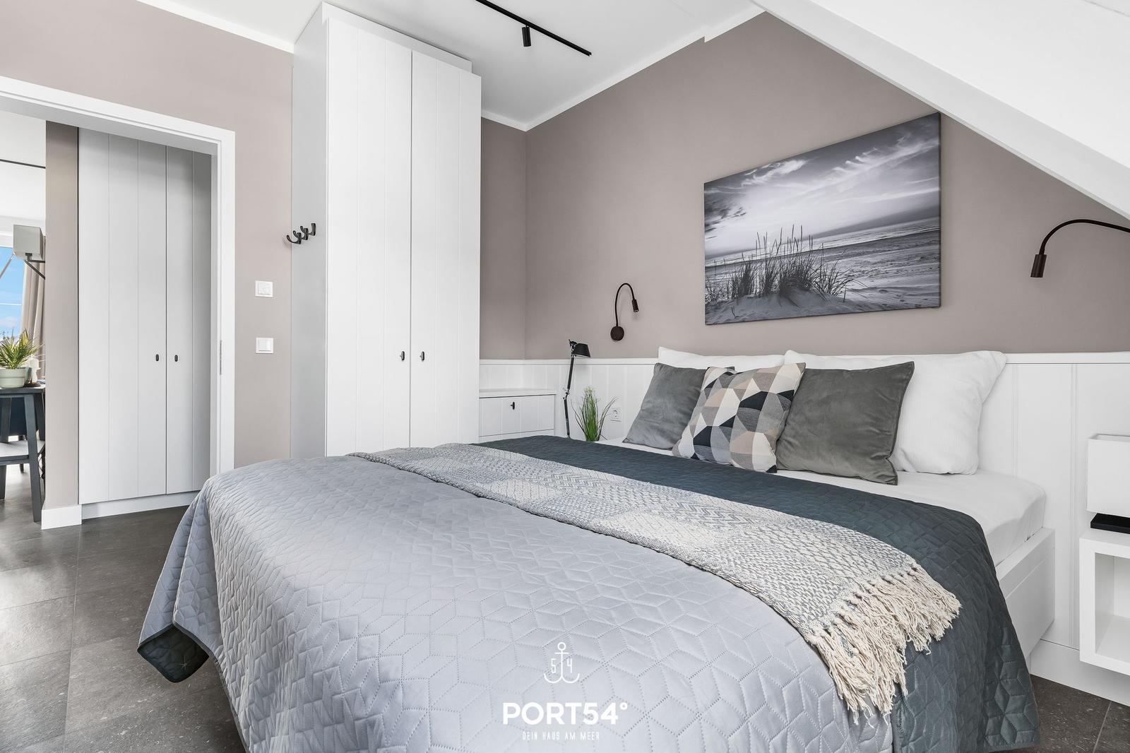 Schlafzimmer mit Bett, Kleiderschrank und Wandbild. Dachschrägen und neutrale Farben.