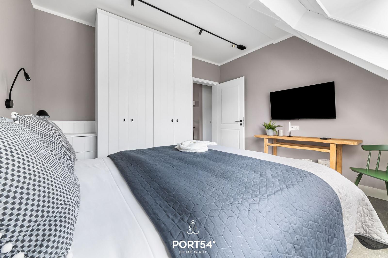 Schlafzimmer mit Bett, Kleiderschrank und Fernseher an der Wand.