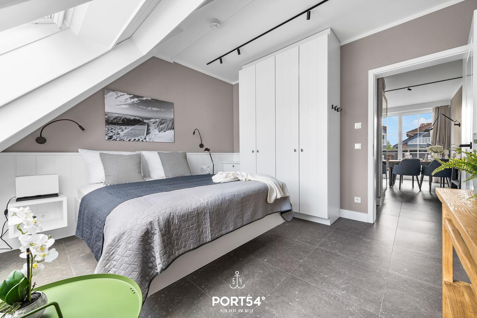 Schlafzimmer mit Dachschrägen, Bett, Kleiderschrank und Blick in Wohnbereich.