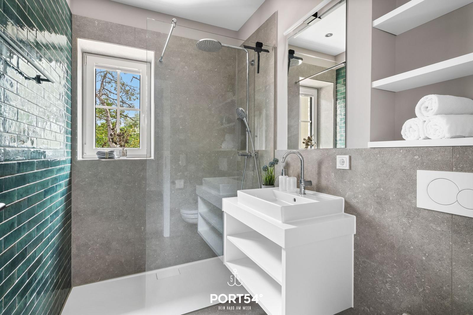 Bad mit Dusche, Waschbecken und Fenster mit Blick auf Bäume.