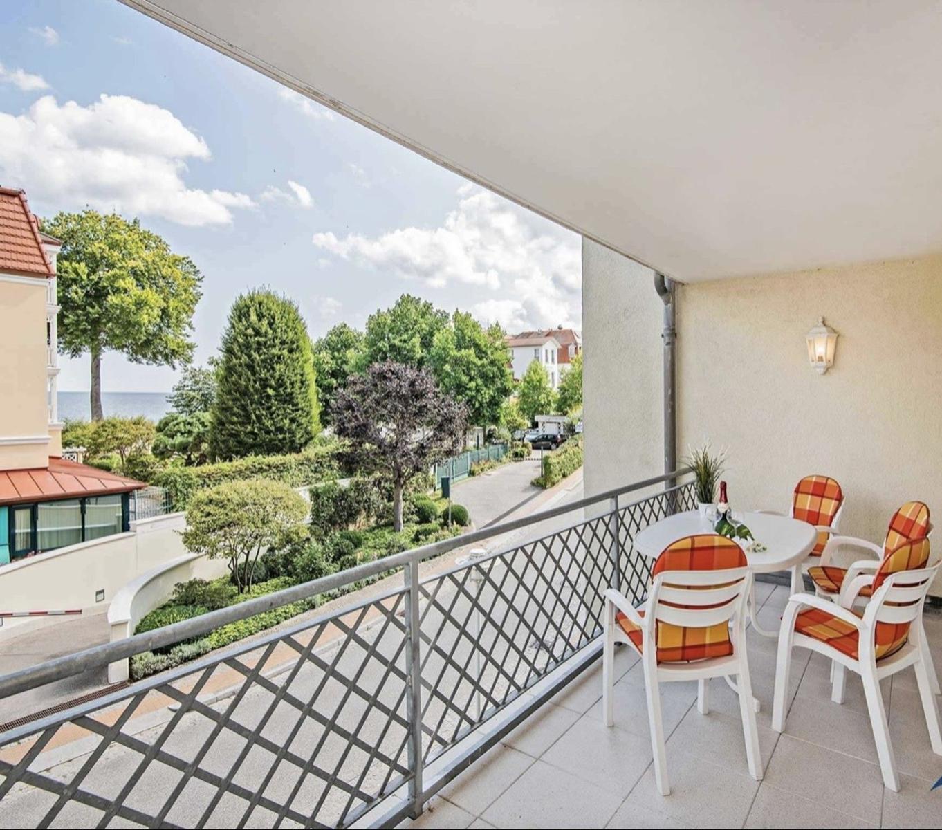 Terrasse mit Tisch und Stühlen, Blick auf Grünanlagen und Meer.