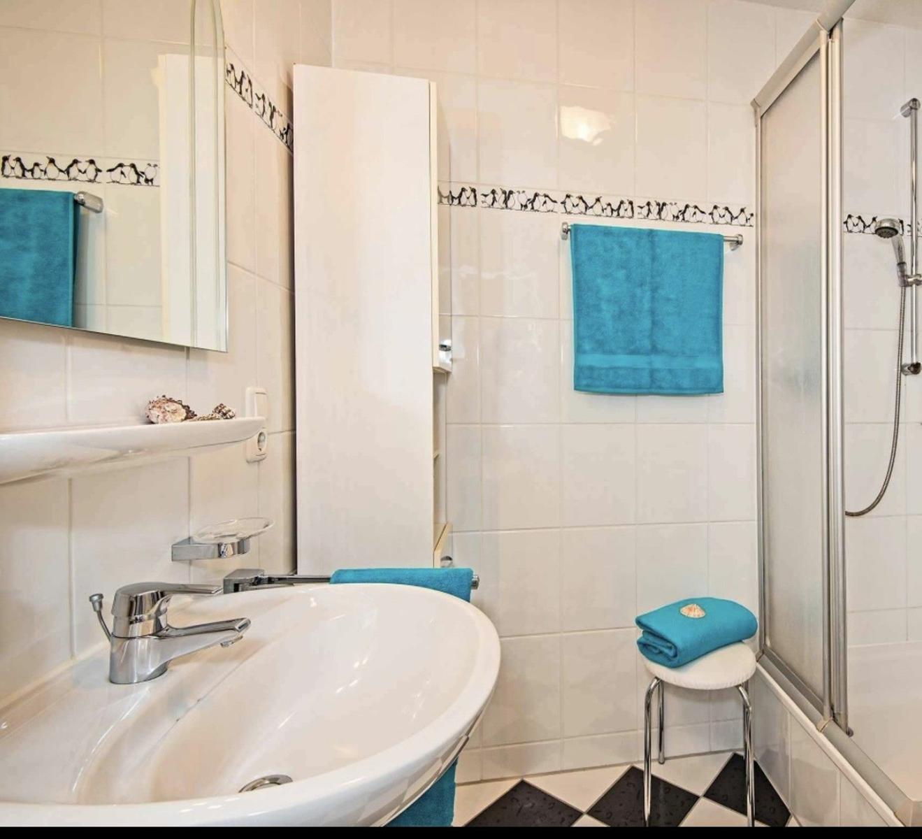 Badezimmer mit Dusche, Waschbecken und blauen Handtüchern.