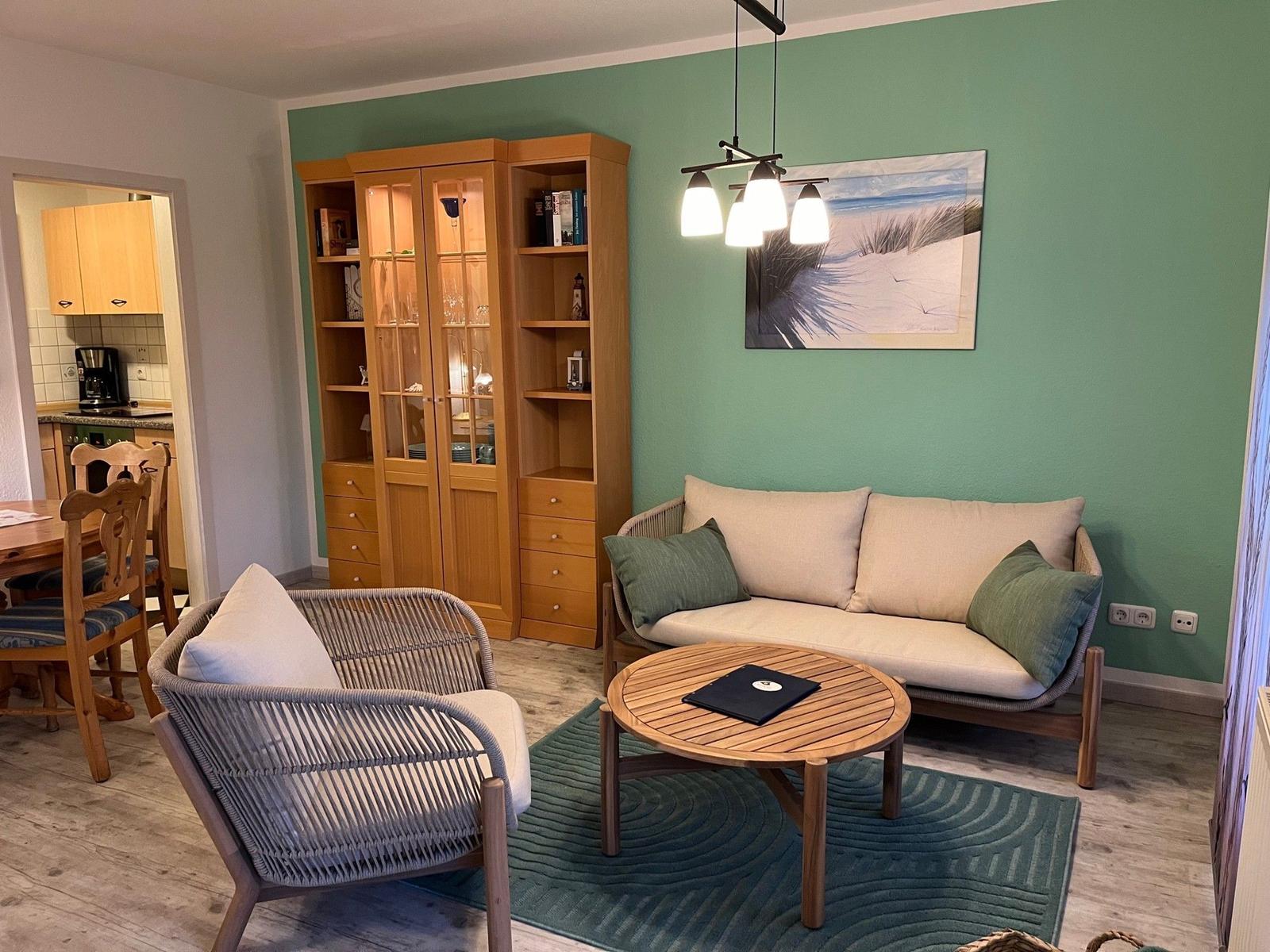 Wohnzimmer mit Sofa, Sessel und Holzregal an grüner Wand.