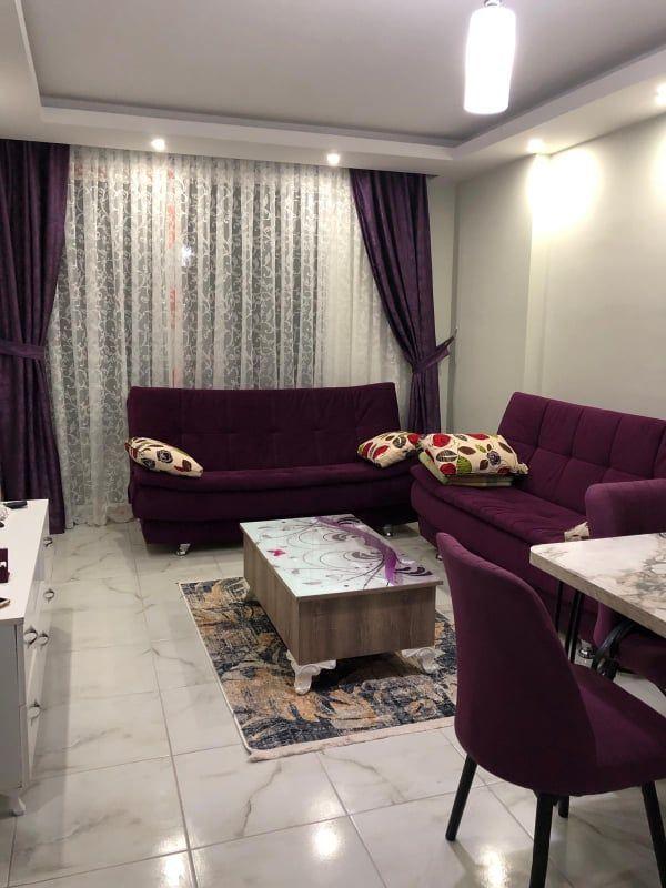 Wohnzimmer mit lila Sofa, Tisch und Teppich auf Marmorfliesen.