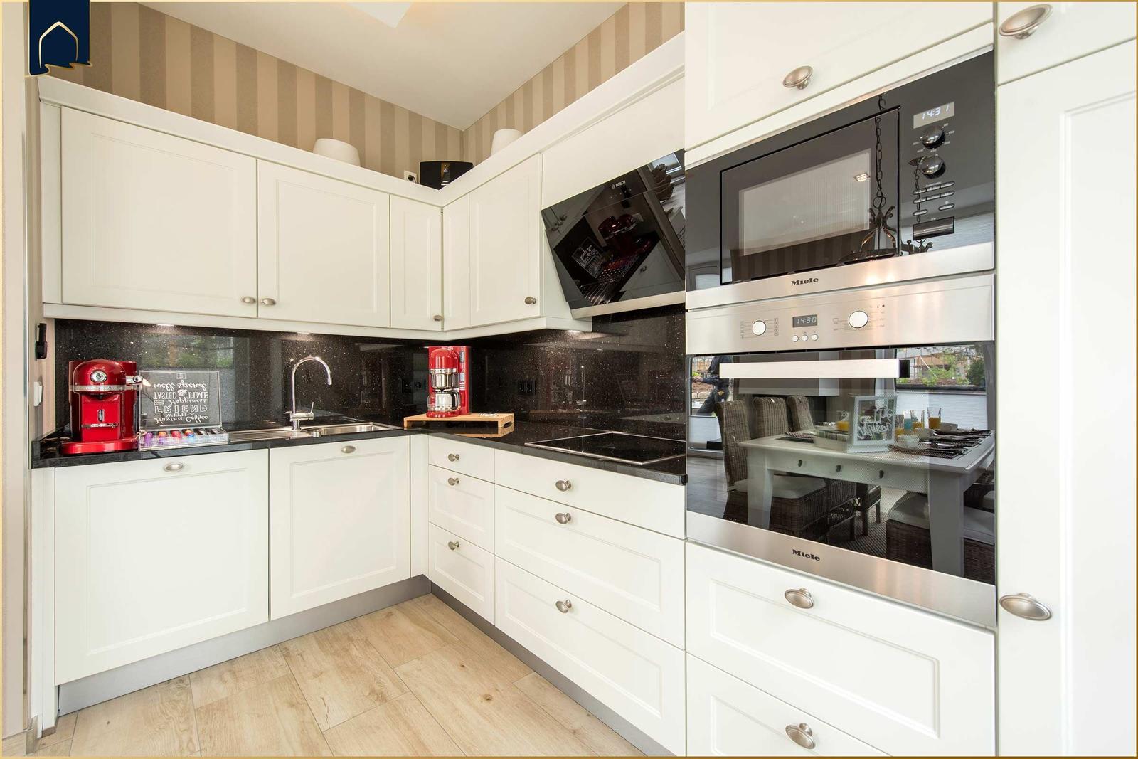 Küche mit weißen Schränken, schwarzer Arbeitsplatte und integriertem Herd.