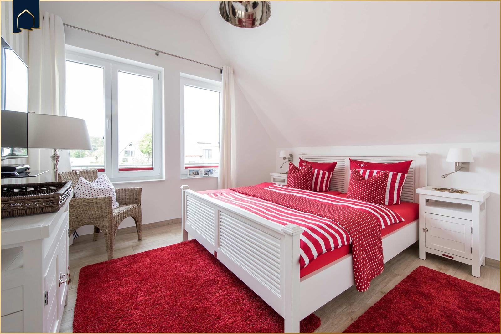 Schlafzimmer mit weißem Bett, rotem Teppich und Fenstern mit Blick nach draußen.