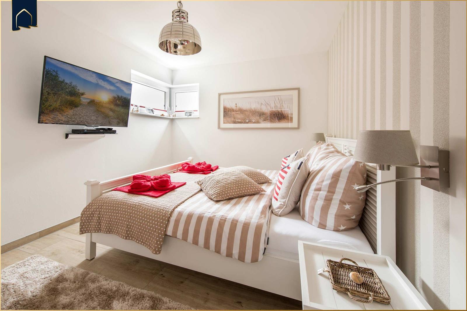 Schlafzimmer mit Bett, Fernseher und Wandlampe. Wand mit Streifen, Bild und Fenster.