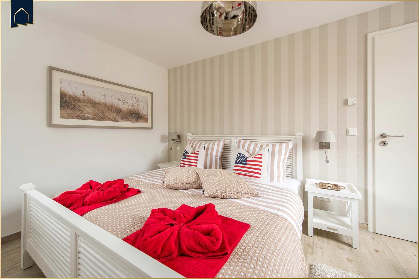 Schlafzimmer mit weißem Bett, gestreifter Wand und roten Handtüchern.