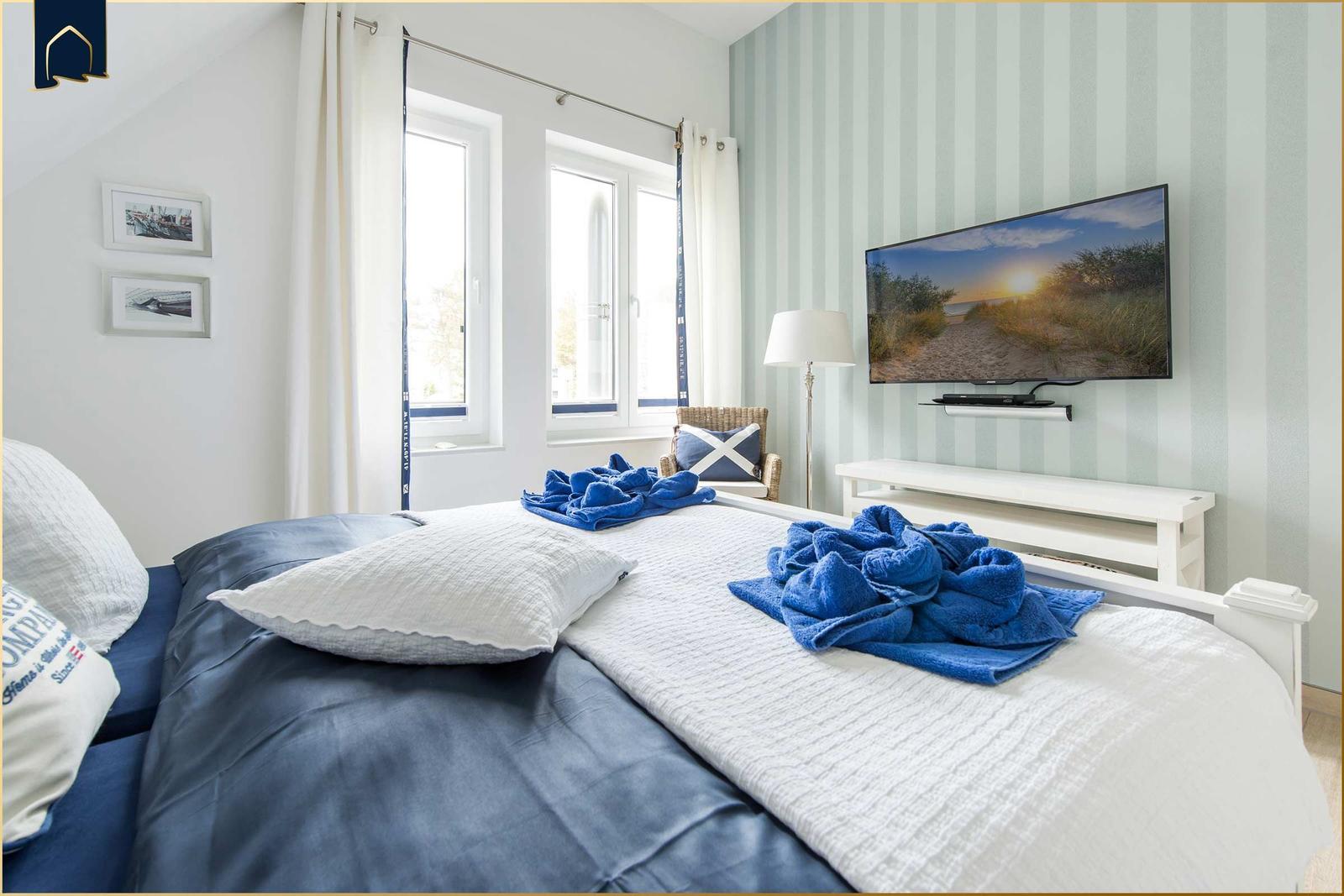 Schlafzimmer mit Bett, TV und Fenstern.