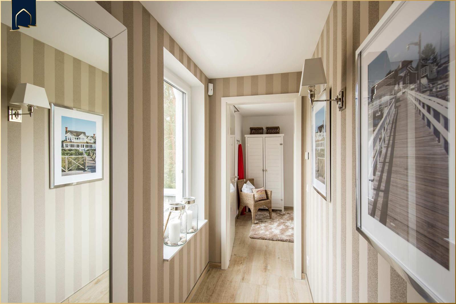Flur mit Streifenwand, Fenster, Bildern und Blick in Schlafzimmer mit Schrank und Stuhl.