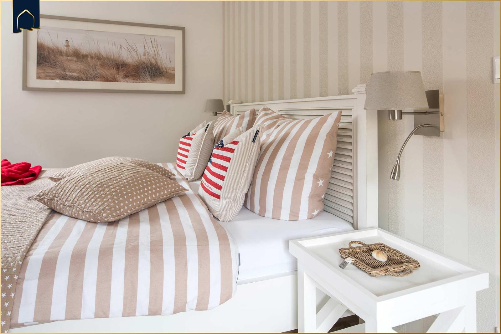 Ein Bett mit Streifenbezug und Kissen, daneben Nachttisch und Wandlampe.