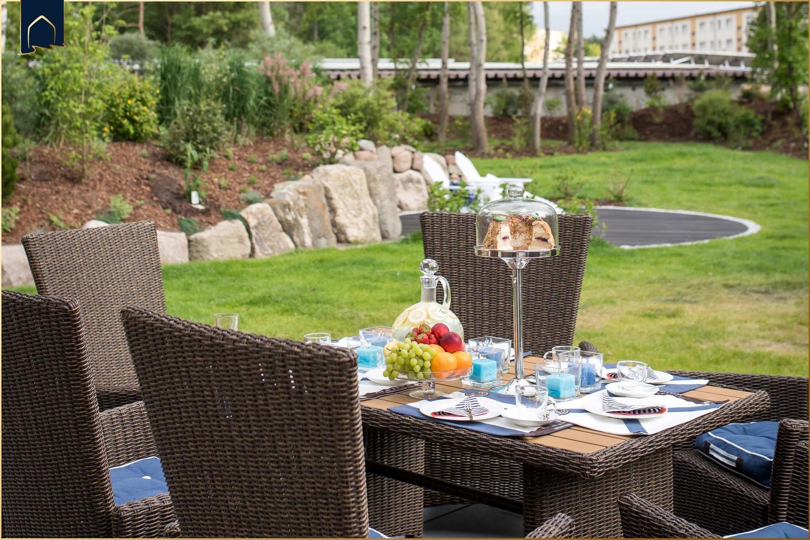 Garten mit gedecktem Tisch, Stühlen und Obst. Hintergrund: Rasen, Steine und Bäume.