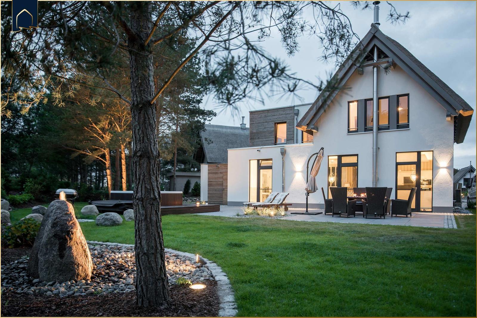 Modernes Haus mit Terrasse, Garten und Grillplatz bei Abenddämmerung.