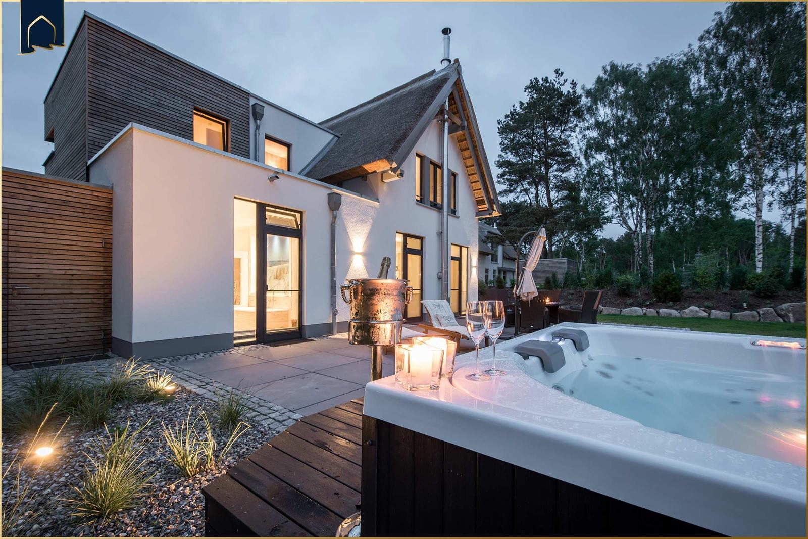 Modernes Haus mit Whirlpool, Terrasse und Garten bei Dämmerung.