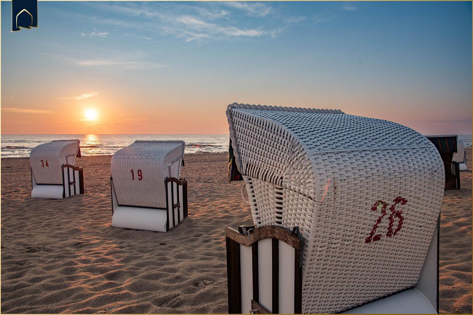 Drei weiße Strandkörbe stehen am Strand bei Sonnenuntergang.