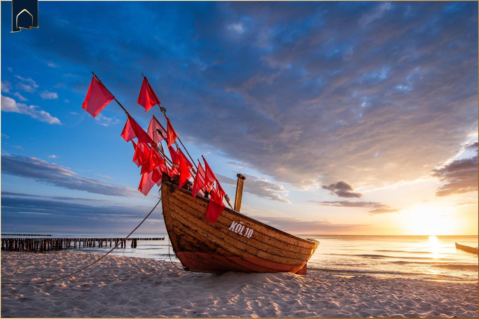 Ein hölzernes Boot mit roten Flaggen steht am Strand bei Sonnenuntergang.
