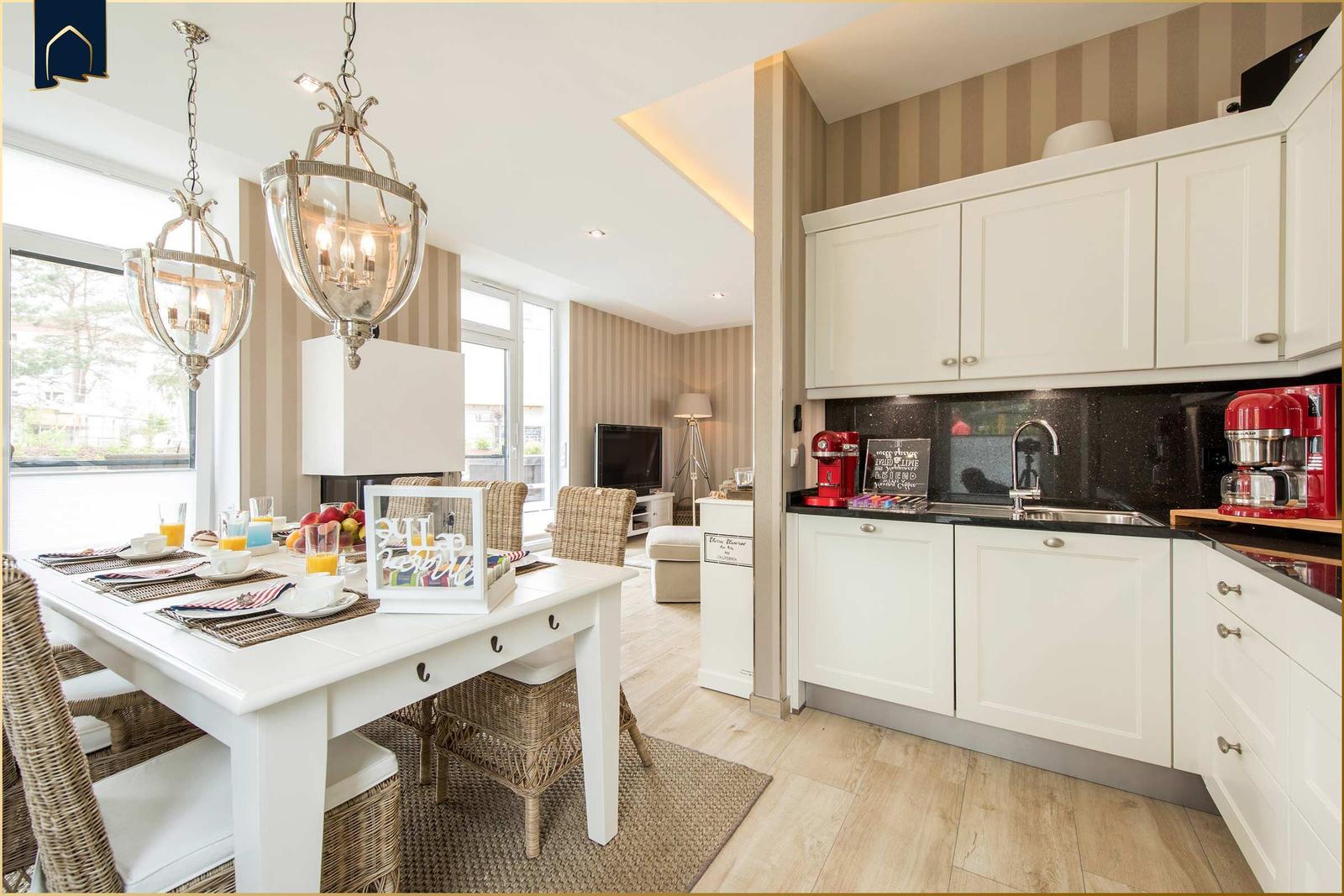 Essbereich mit weißem Tisch und Stühlen. Küche mit weißen Schränken und rotem Küchenapparat.