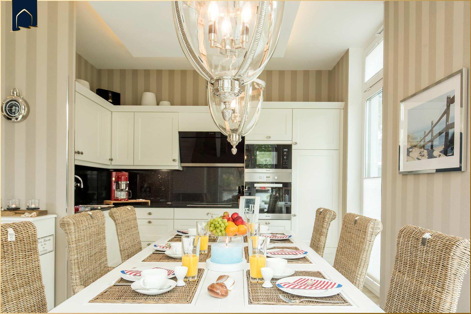 Esszimmer mit Esstisch, Stühlen und Küchenbereich im Hintergrund.