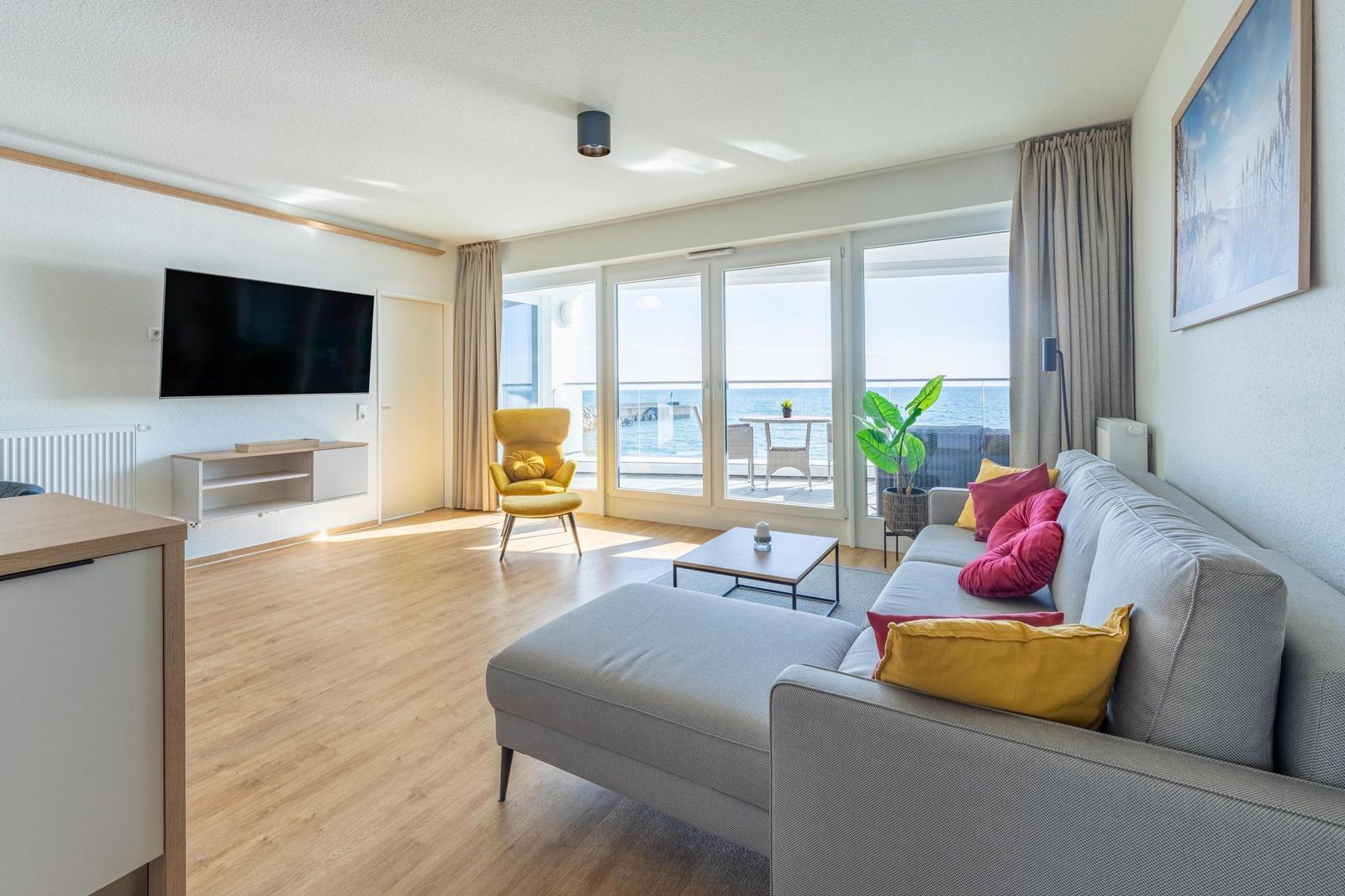 Wohnzimmer mit Sofa, Fernseher und Meerblick durch große Fenster.