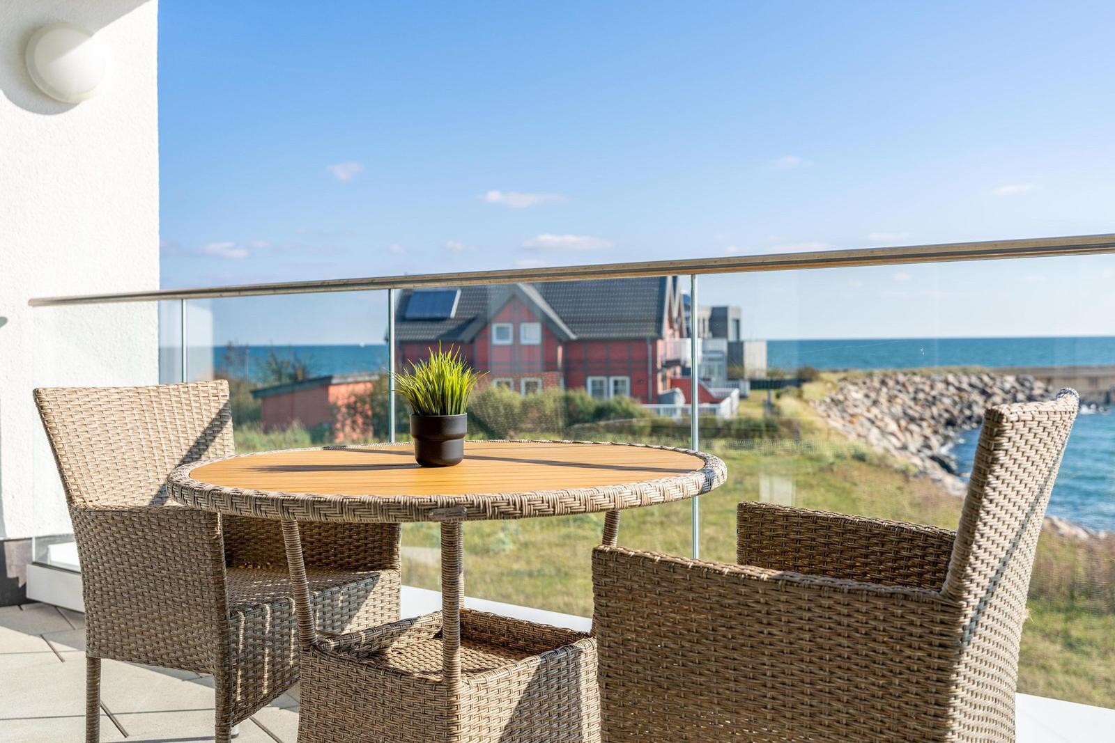 Terrasse mit Tisch und Stühlen, Blick auf Meer und rotes Haus.