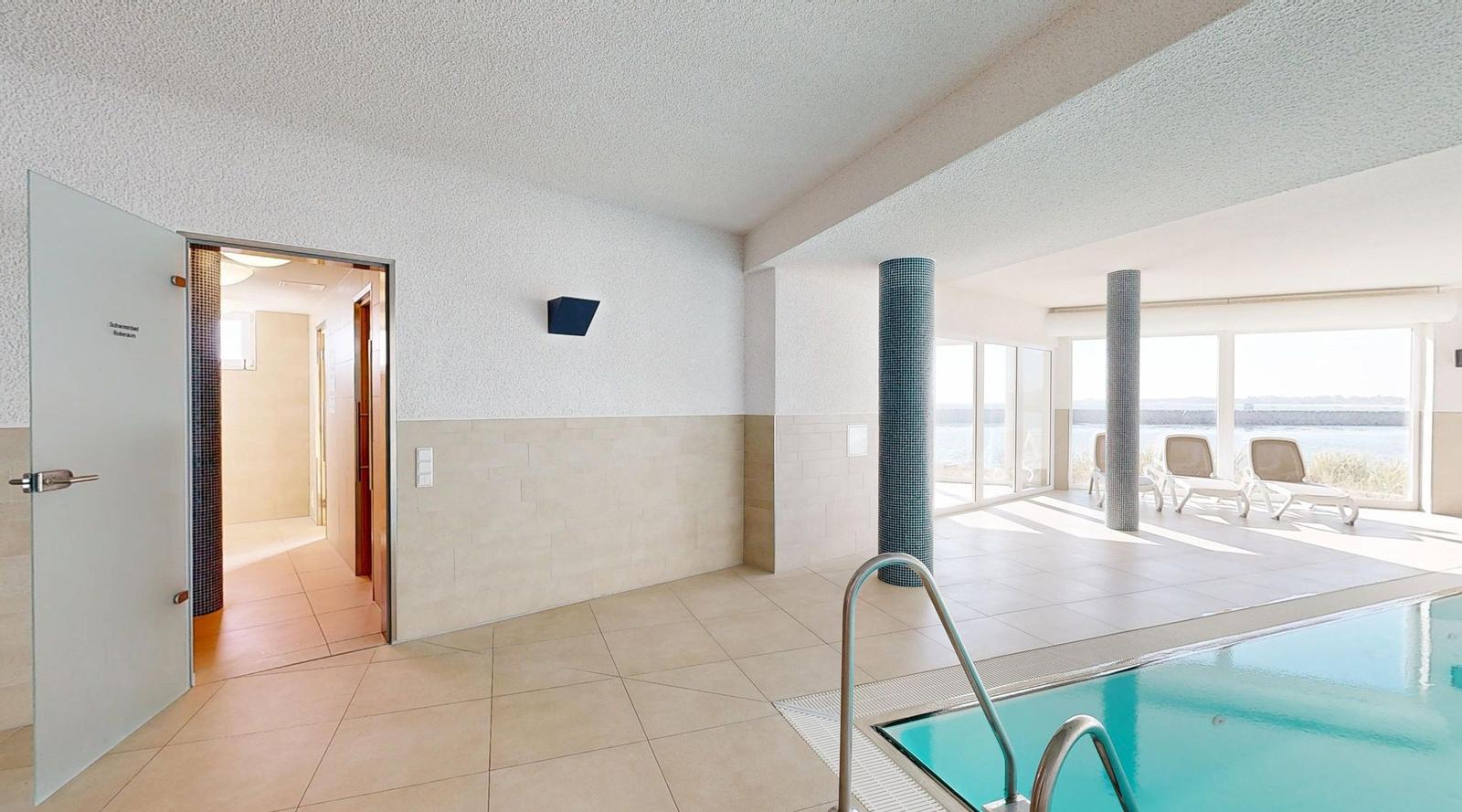 Innenpool mit Außenterrasse und Liegestühlen. Tür führt in Dampfbad.