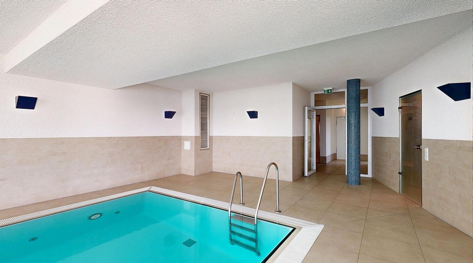 Innenpool mit Metalltreppe und hellen Wänden. Türen und Säulen sind sichtbar.