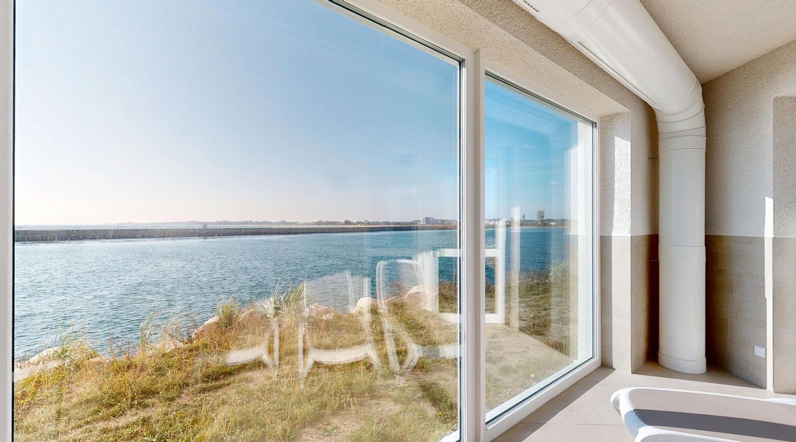 Großes Fenster mit Meerblick auf einen Steg und Wasser.