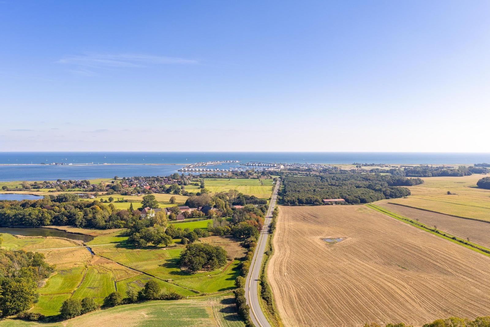 Ausblick auf Küstenlandschaft mit Feldern, Wald und Hafen.
