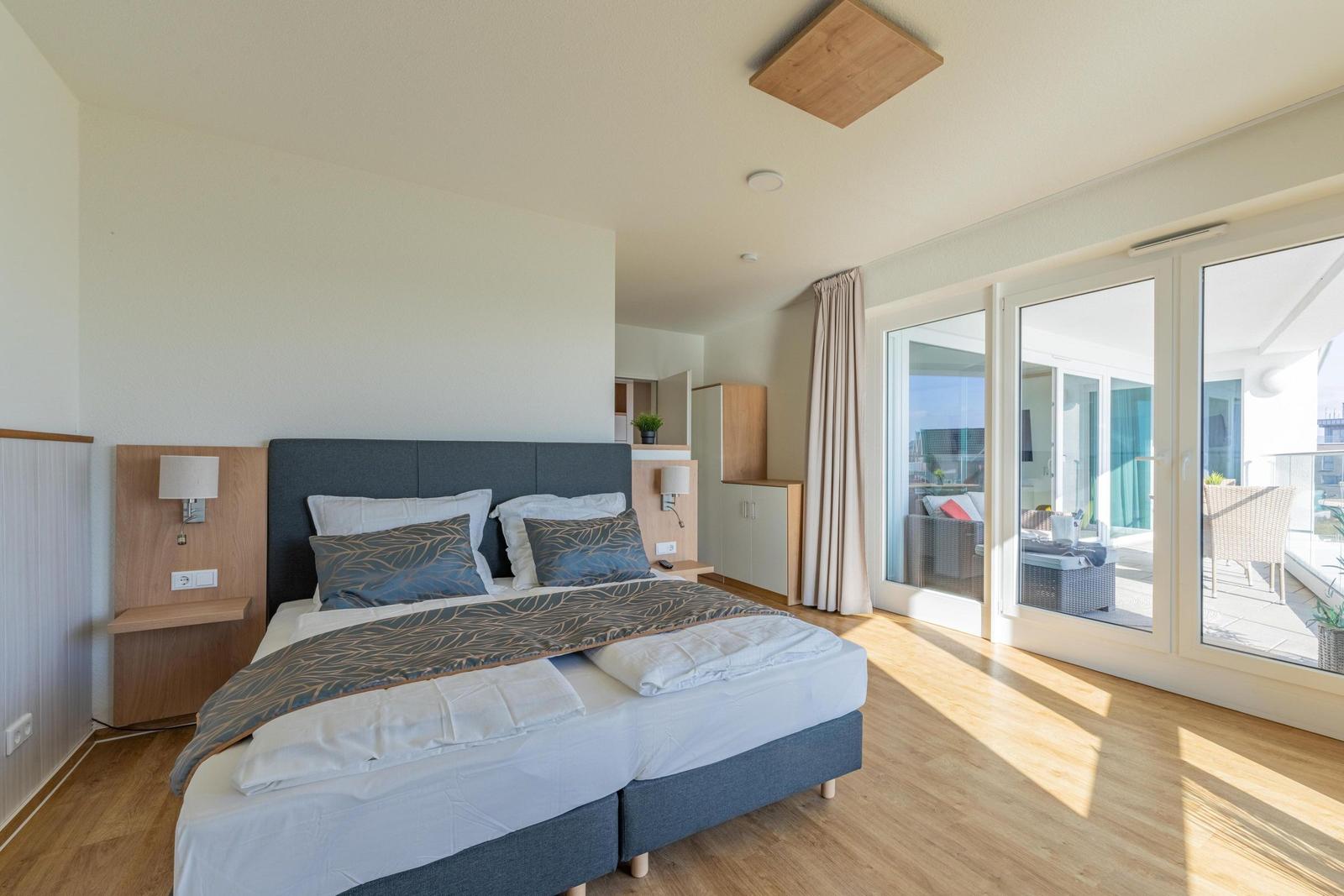 Schlafzimmer mit Doppelbett, Balkon und Holzboden.