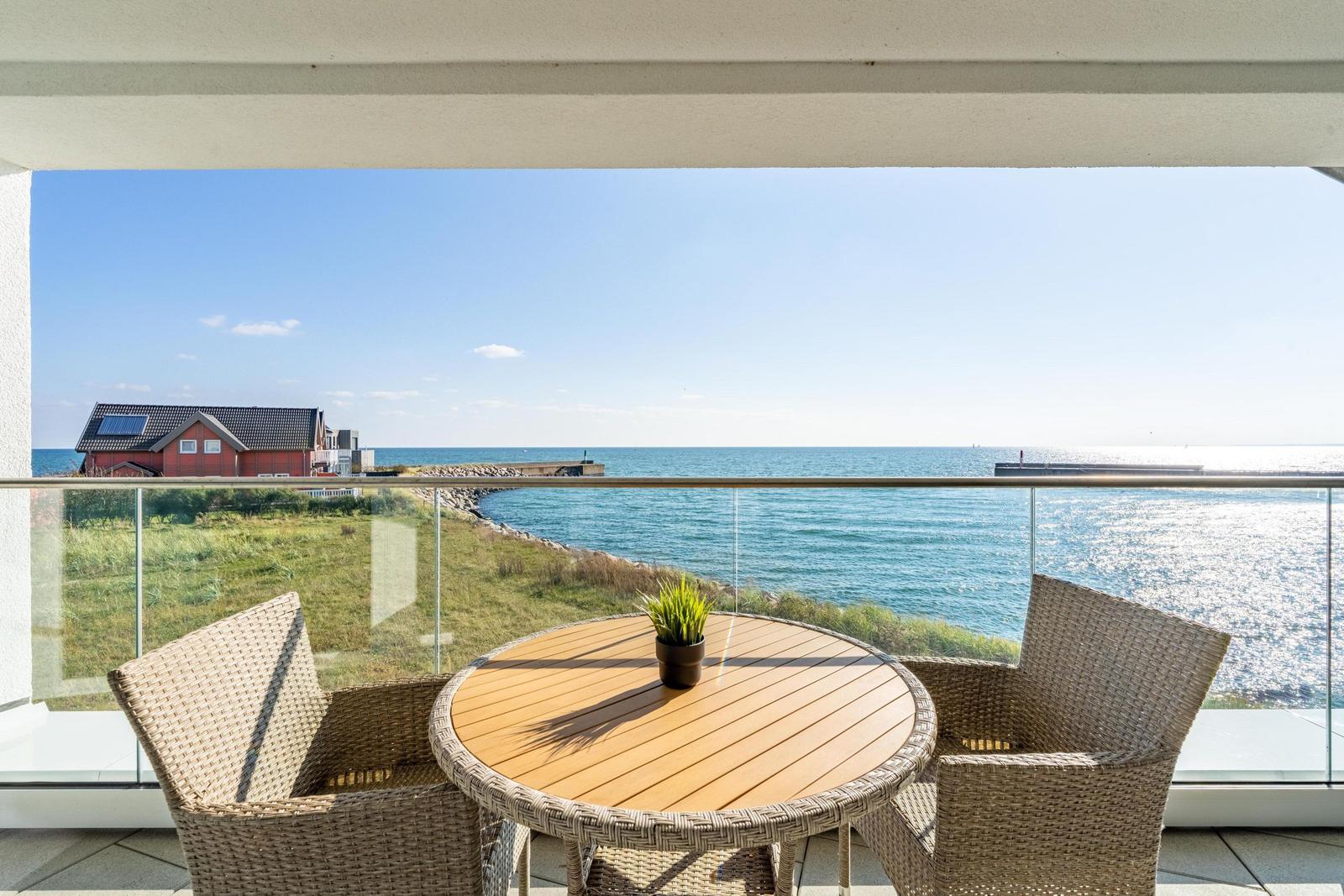 Terrasse mit Tisch und Stühlen bietet Blick auf Meer und Strandhaus.