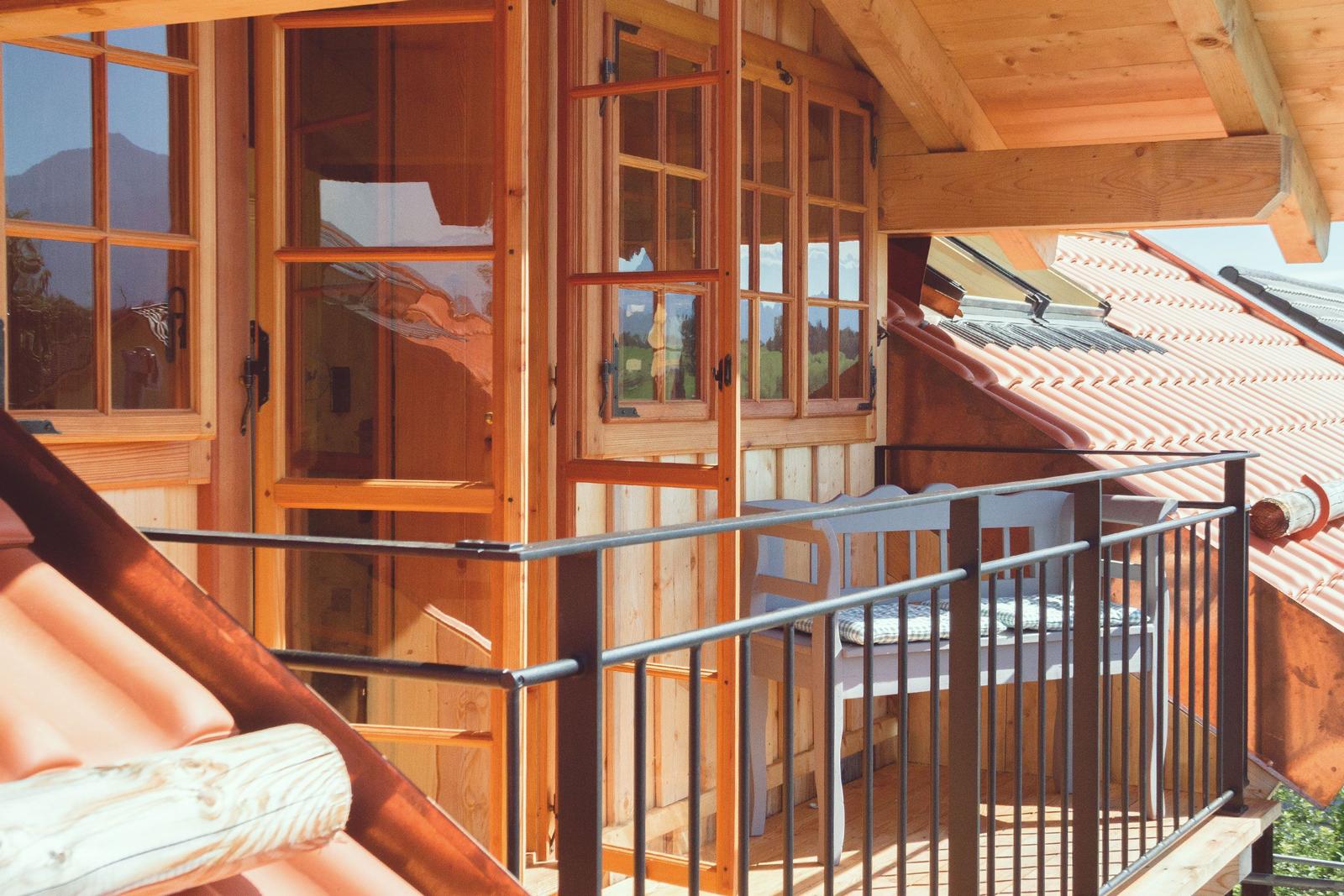 Terrasse mit Holzgeländer und Sitzbank unter Dach, Blick auf Dachziegel und Berge.